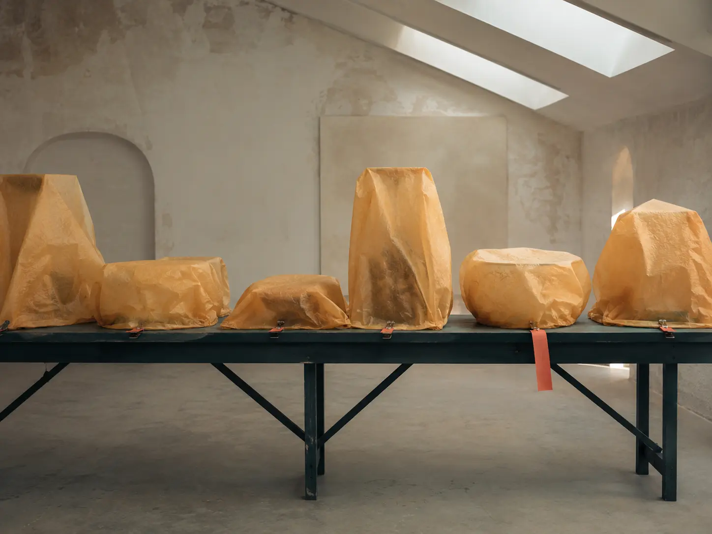 Display objects concealed beneath translucent amber paper on a long dark teal table